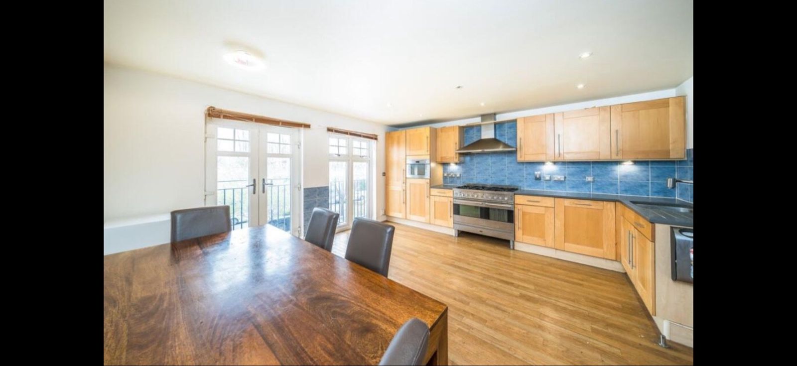 Wood-cabinet kitchen with gas range, blue tile splashback, and French doors opening onto a Juliet balcony