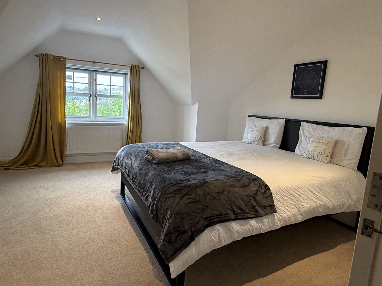 Master bedroom with mustard curtains, framed star map, and a leafy view from the window