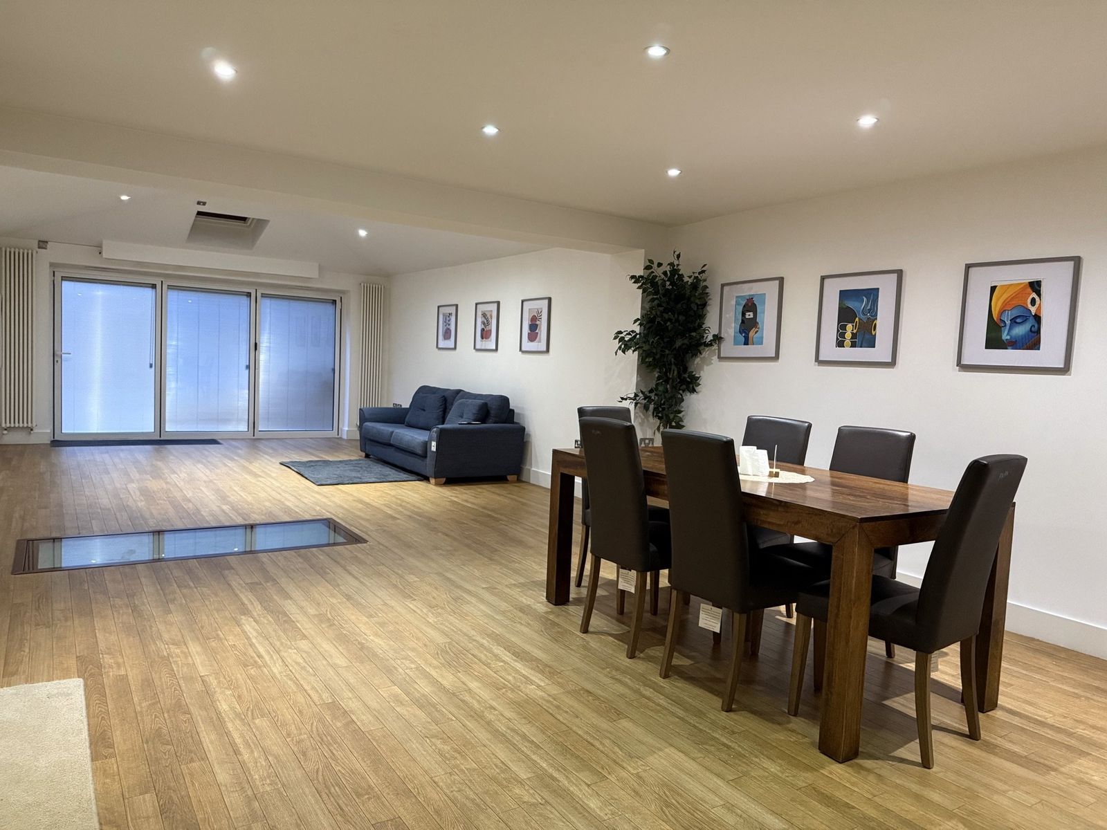 Open-plan main living and dining room with skylights, blue sofas, art gallery wall, and a long wooden dining table