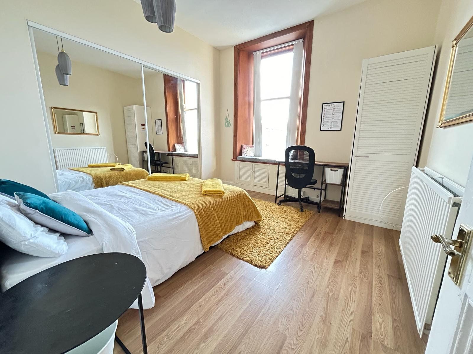 Bedroom alternative angle — bed with mustard textiles, work desk, mirrored wardrobe, period sash window